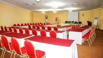 A conference room with rows of tables and chairs, a projector screen, and a podium.