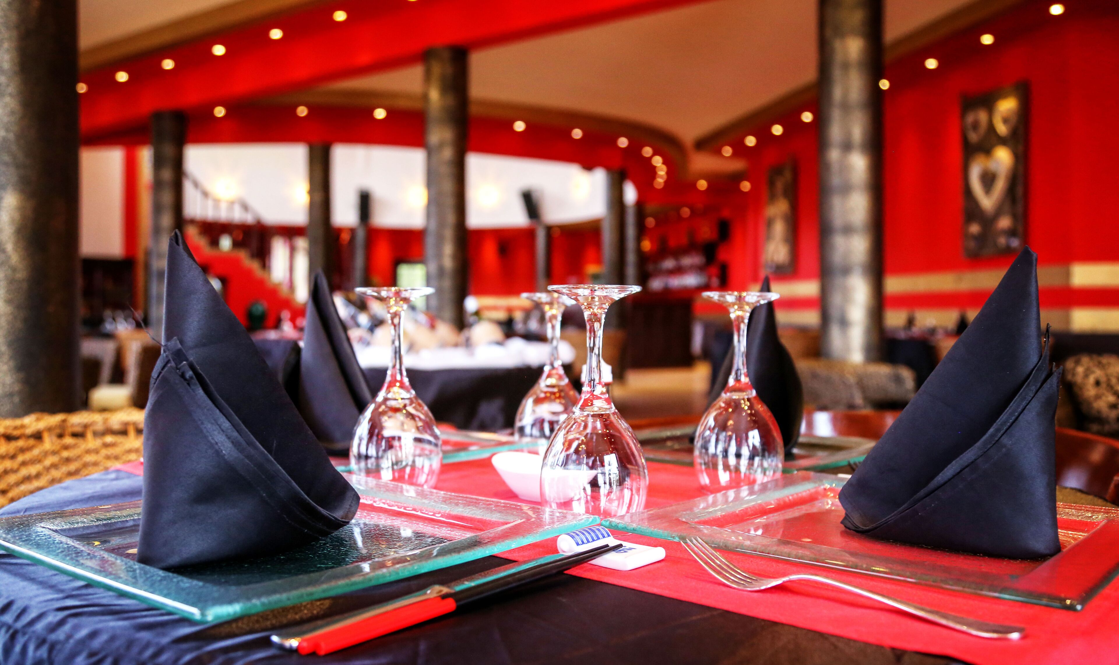 Un restaurante con una mesa dispuesta para dos, con vasos transparentes y servilletas negras.