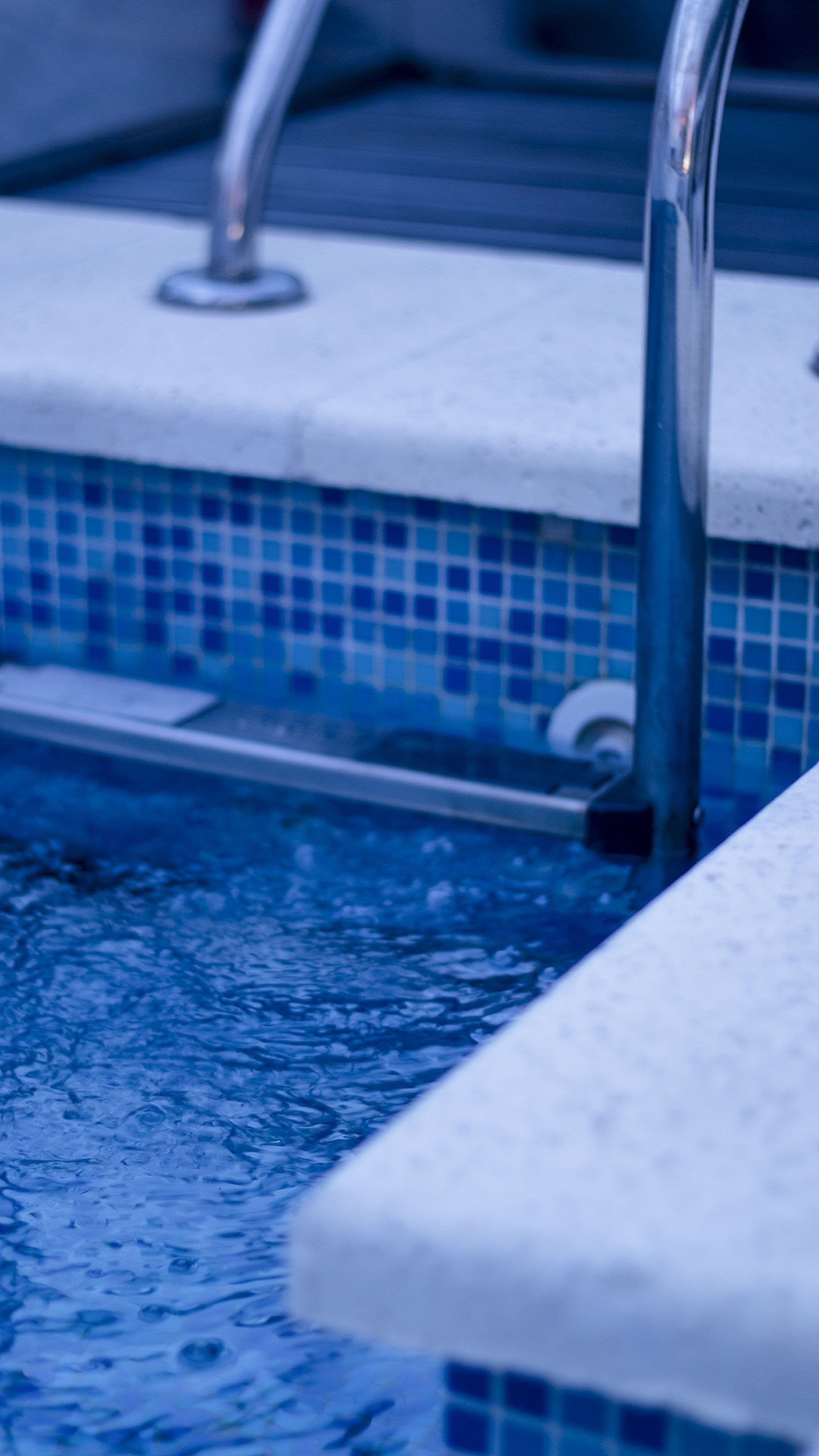 A pool with a tiled edge and a metal handrail.