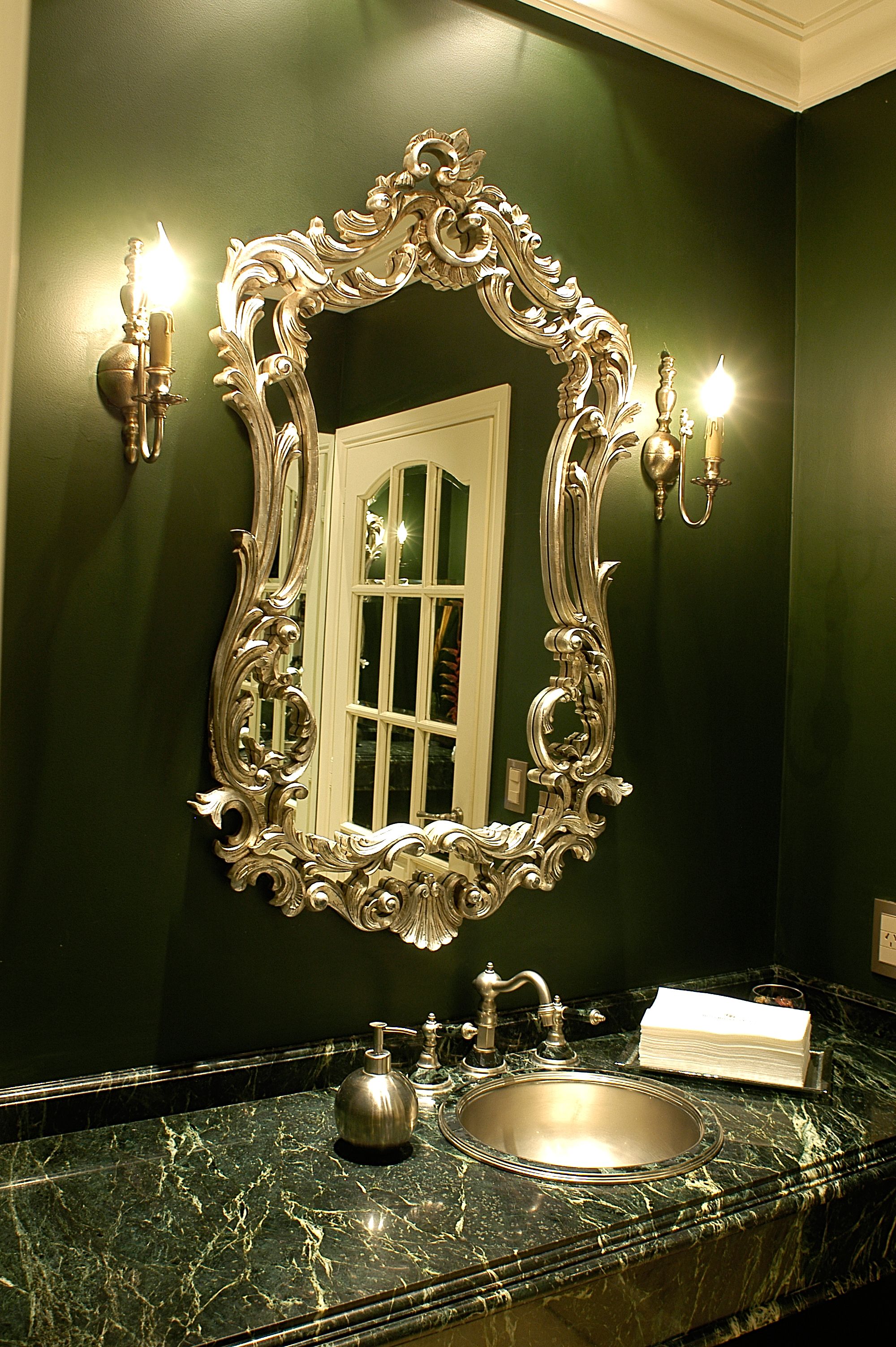 A bathroom with a large ornate mirror, a sink, and two wall-mounted lights.