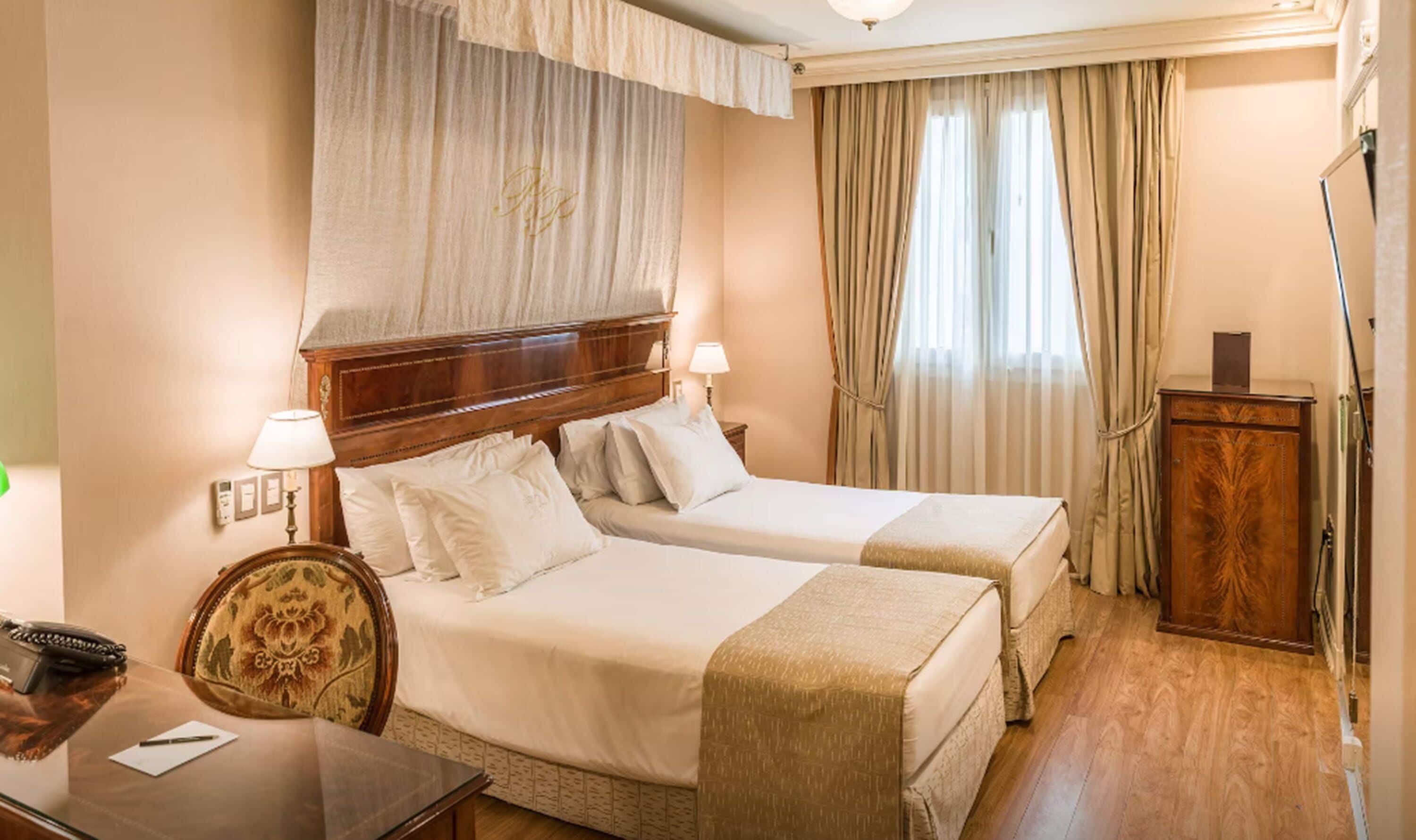 Habitación de hotel con dos camas, un cabecero de madera, un escritorio con teléfono y un armario pequeño.