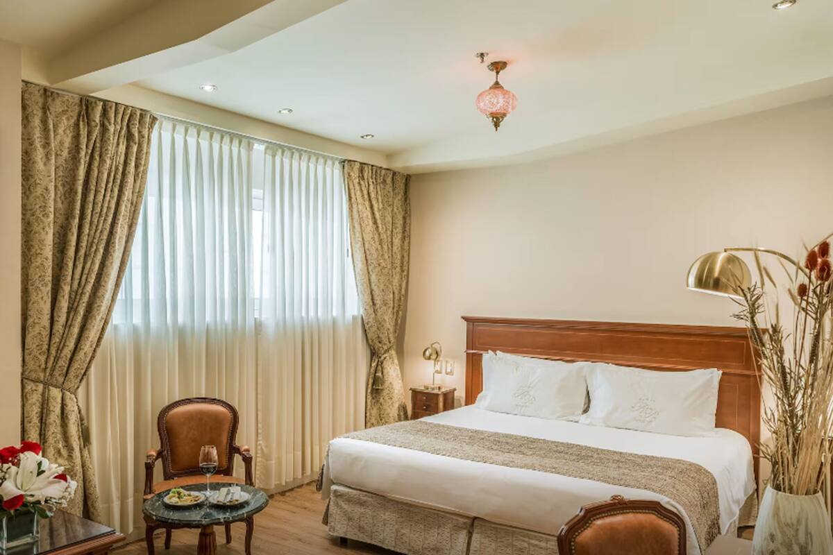 A hotel room with a large bed, a chair, a small table with a vase of flowers, and a lamp.