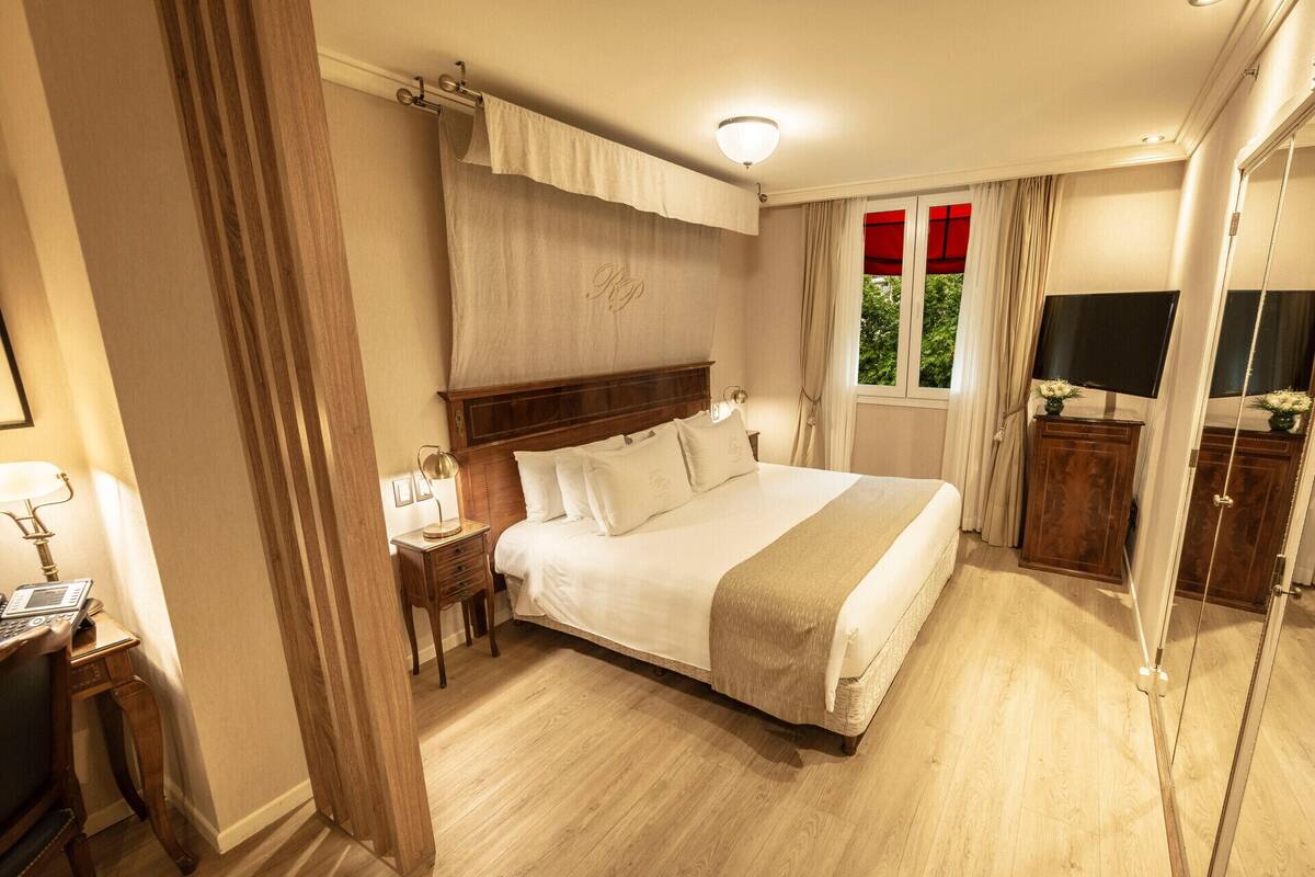 A hotel room with a large bed, bedside tables, a desk, a mirror, and a TV.