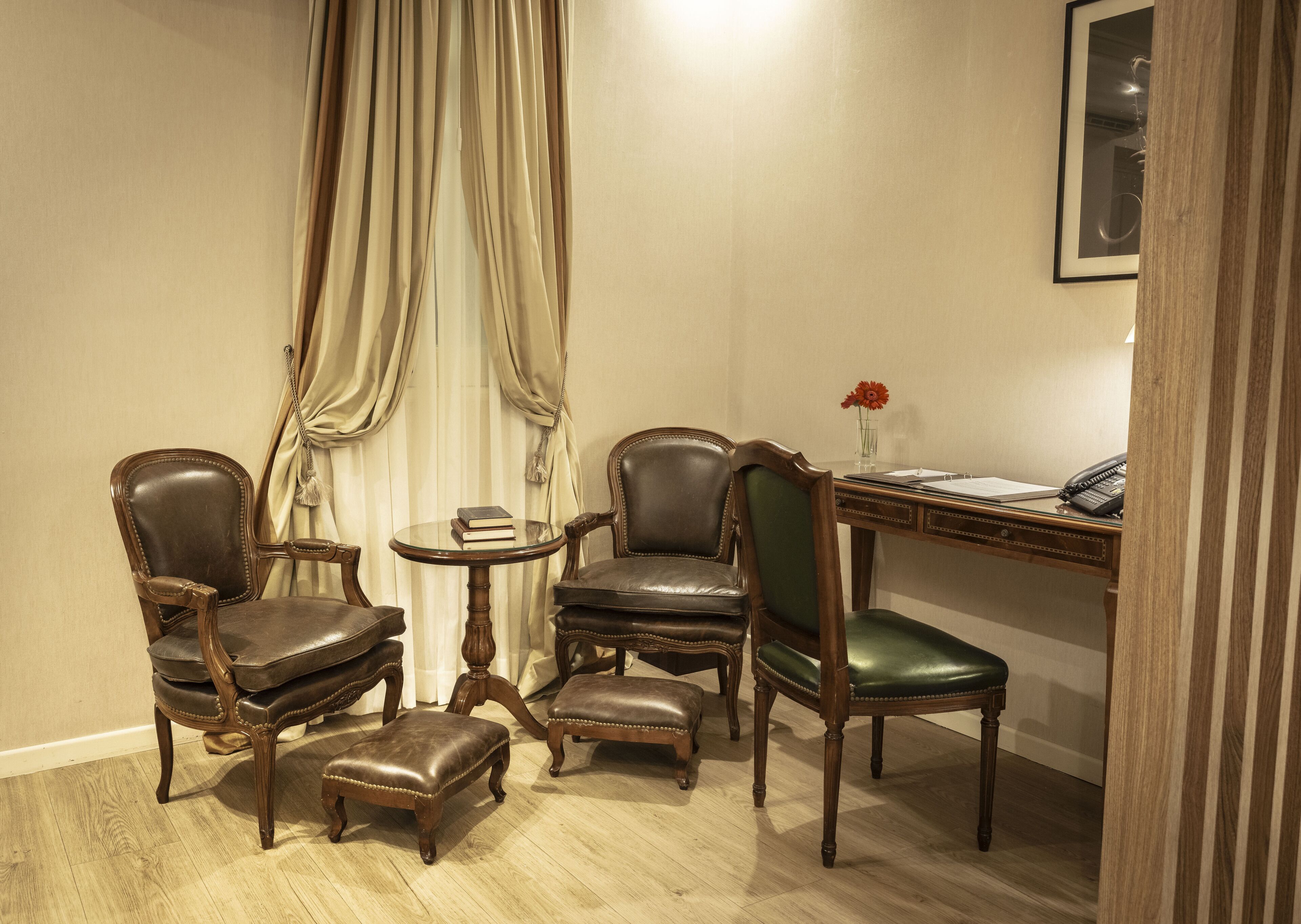 A corner room with a desk, two chairs, a small table, and a chair with a green seat.