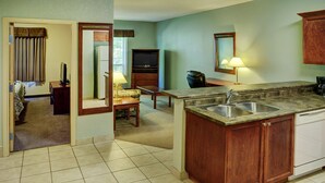 A compact kitchen with a built-in sink, wooden cabinets, a dining area with a table and chairs, and a television in the corner.