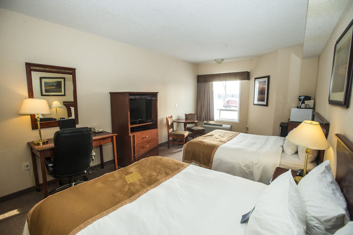 A hotel room with two beds, a desk, a chair, a television, and a window with curtains.