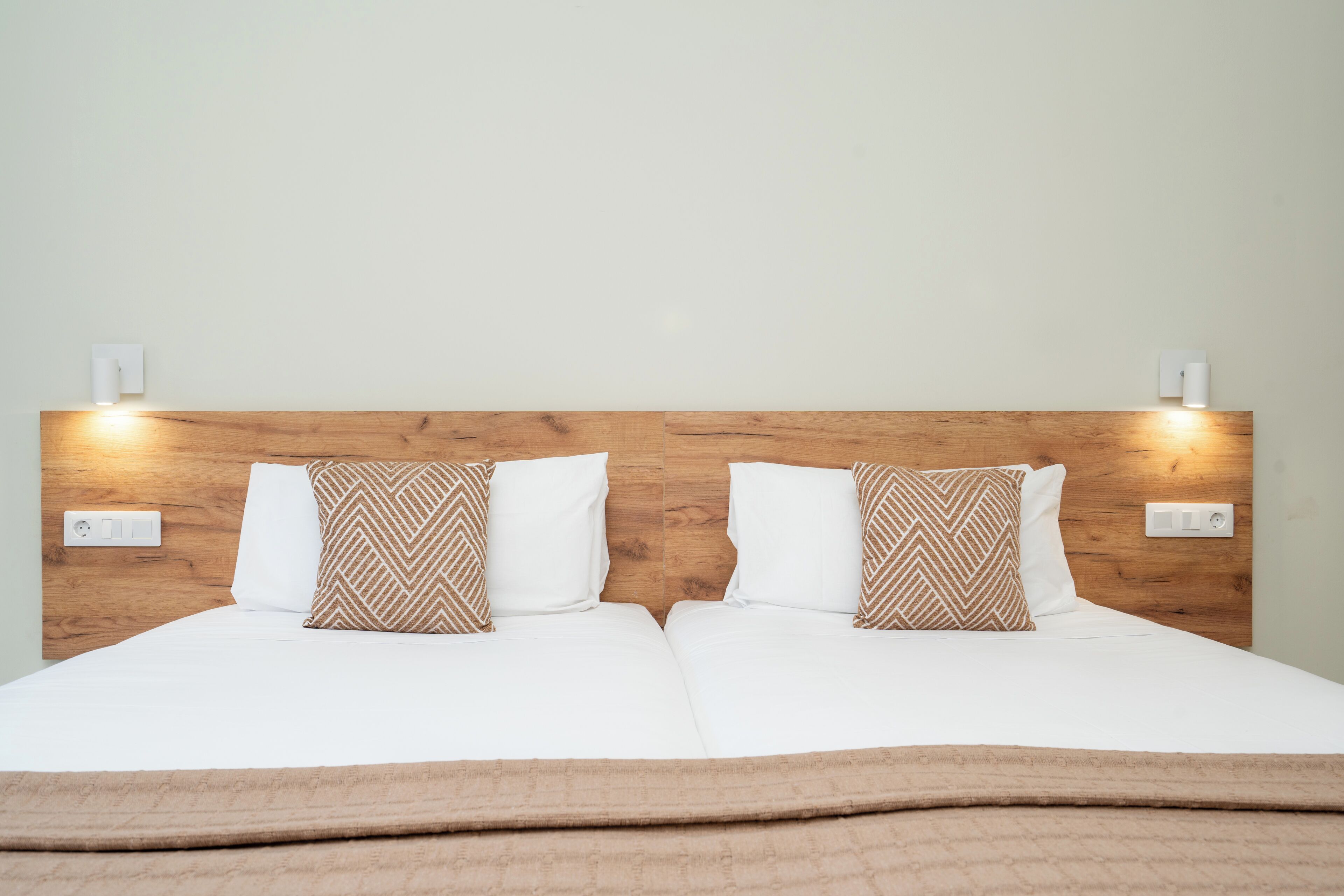 Una cama doble con cabecera de madera, dos almohadas blancas y una manta marrón.