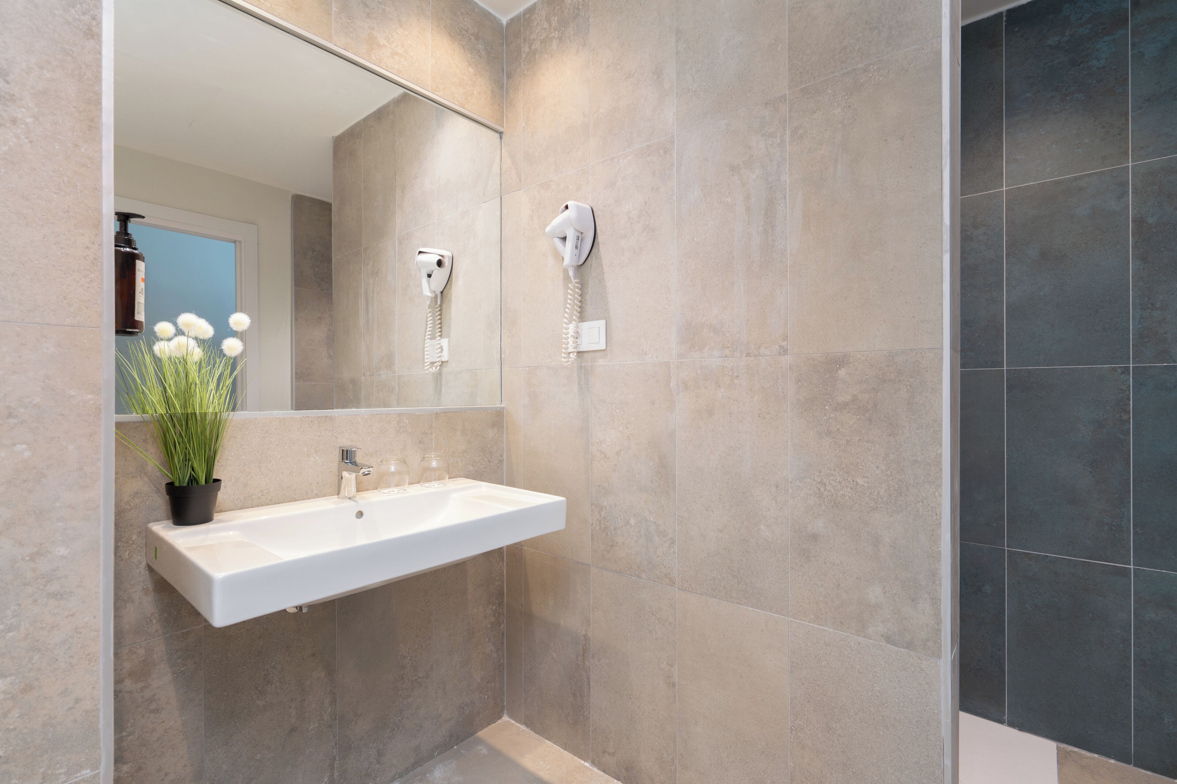 A bathroom with a white sink, a mirror, and a hairdryer mounted on the wall.