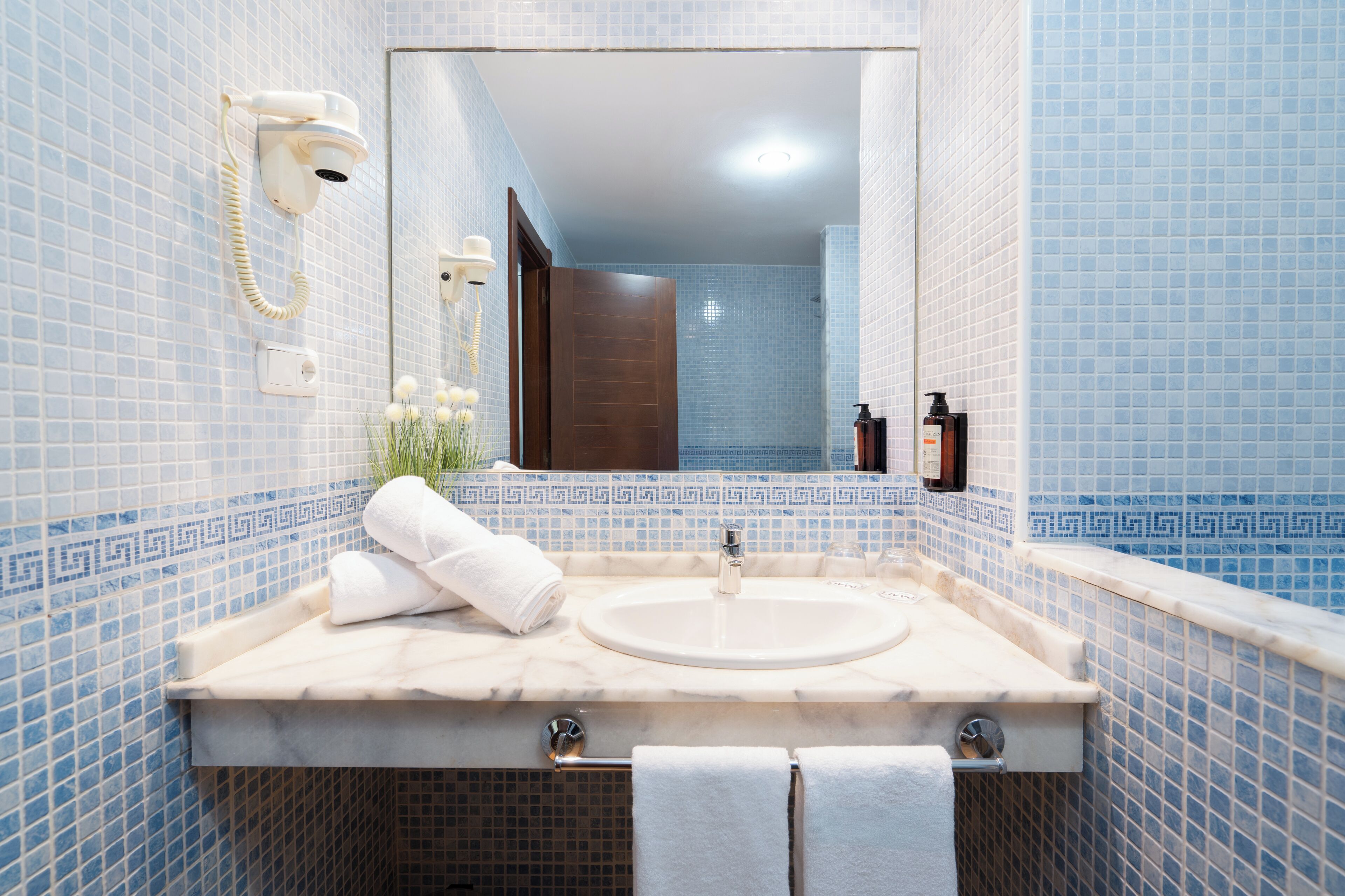 A bathroom with a marble sink, a mirror, a hairdryer, and a towel rack.