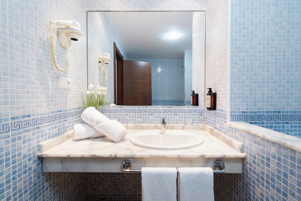 Un baño con lavamanos de mármol, espejo, secador de pelo y toallero.