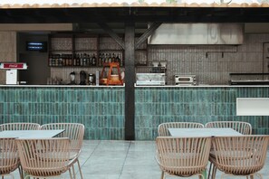 A bar area with a counter, shelves with bottles, a Coca-Cola dispenser, a coffee machine, and wicker chairs. - Hotel LIVVO Jandía Golf - All Inclusive (Pajara)
