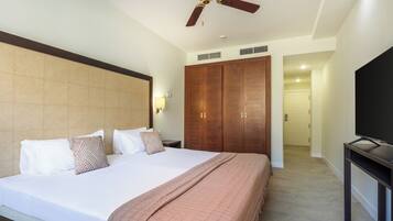 A hotel room with a large bed, wooden wardrobe, ceiling fan, and a TV on a stand.