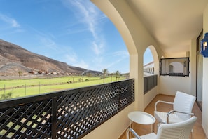 A balcony with a view of a green landscape and distant buildings, white wicker chairs, and a tiled floor. - Hotel LIVVO Jandía Golf - All Inclusive (Pajara)