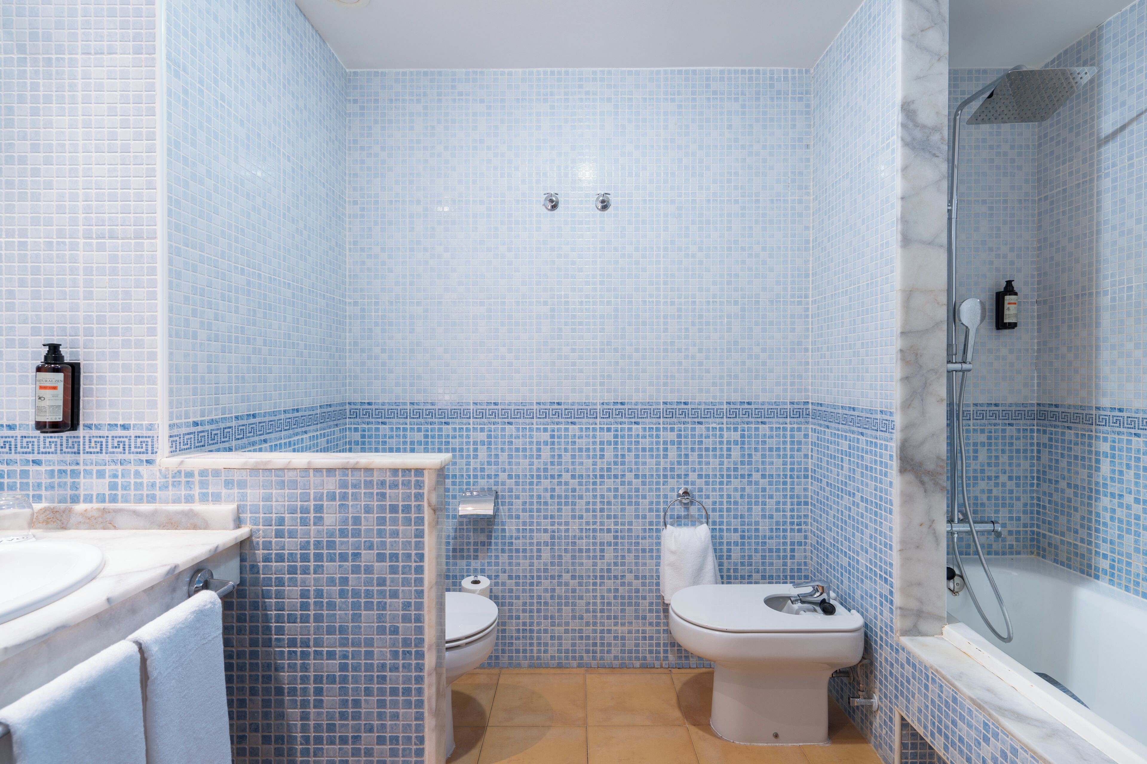 A bathroom with a toilet, bidet, and bathtub, all with blue mosaic tile walls.
