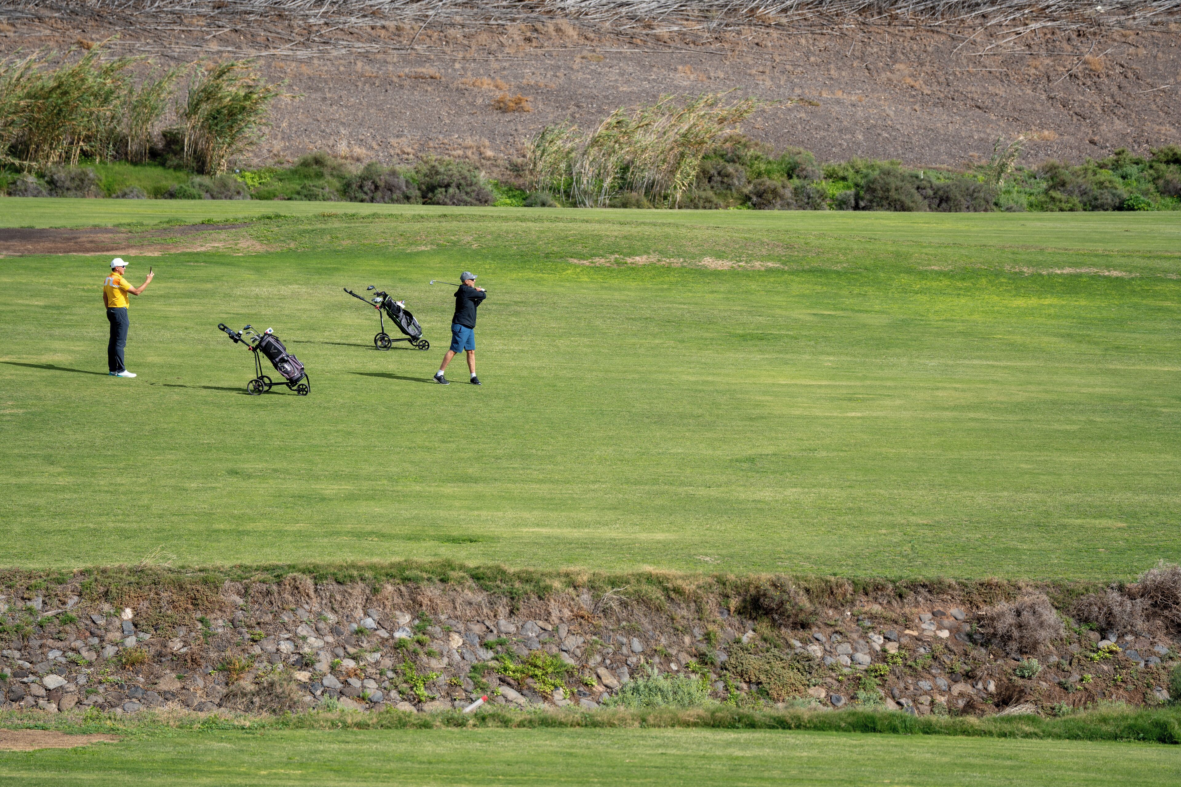 A golf course with a well-maintained green, a rocky embankment, and a clear sky.