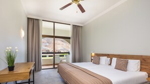 Habitación de hotel con cama, escritorio, planta en maceta y vista a un paisaje urbano a través de amplios ventanales.