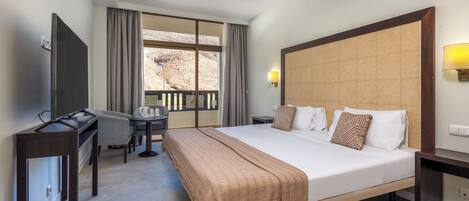 Une chambre d’hôtel équipée d’un lit, d’un bureau, d’une chaise, d’une télévision, d’un ventilateur de plafond et d’une fenêtre donnant sur un paysage agréable.