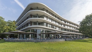 Un edificio moderno de varios pisos con fachada curva, zona de estar al aire libre y un muro de contención de piedra.