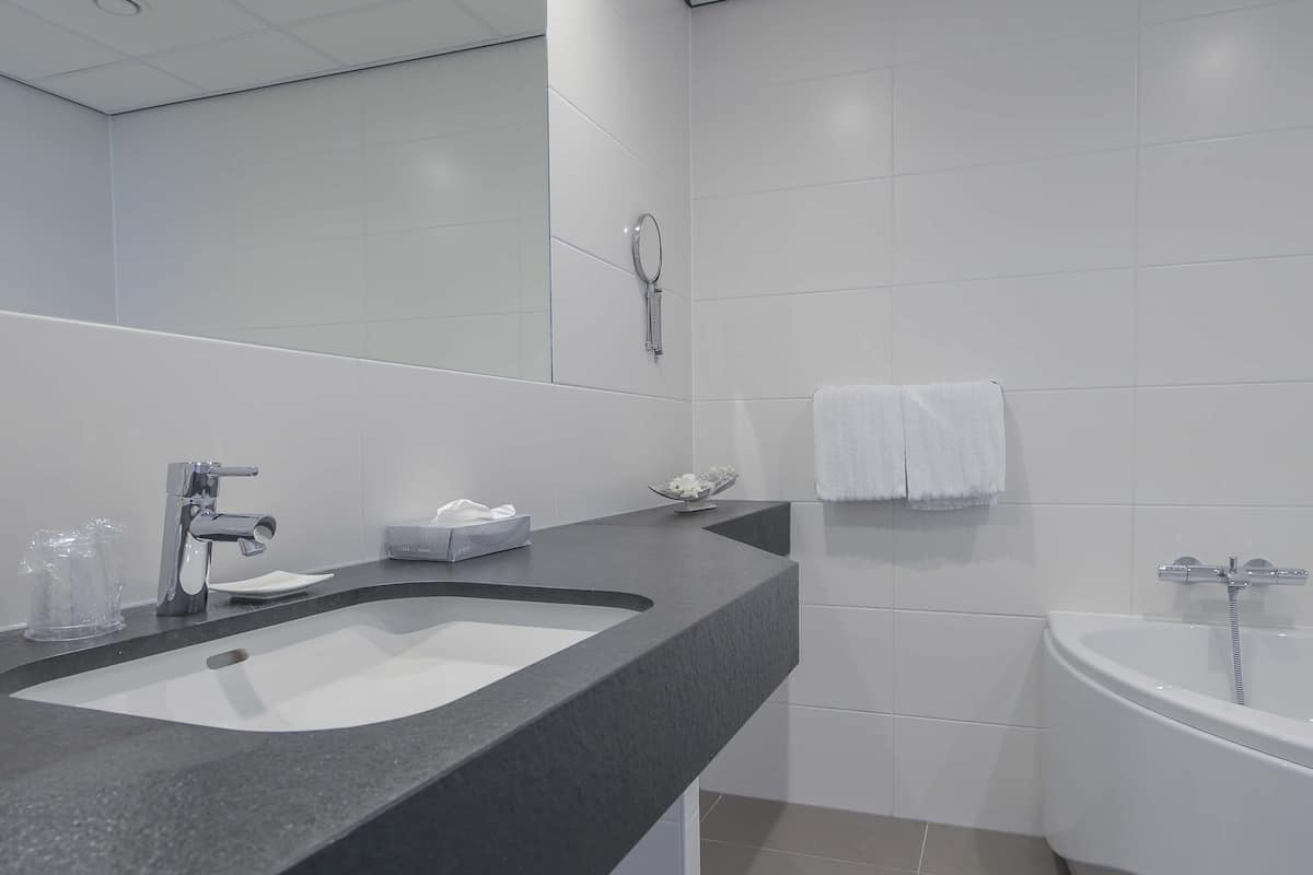 Casa de banho moderna com bancada preta, um espelho grande, lavatório branco, banheira e porta-toalhas.