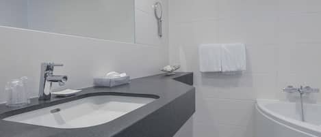Un baño moderno con encimera negra, un espejo grande, lavabo blanco, bañera y toallero.