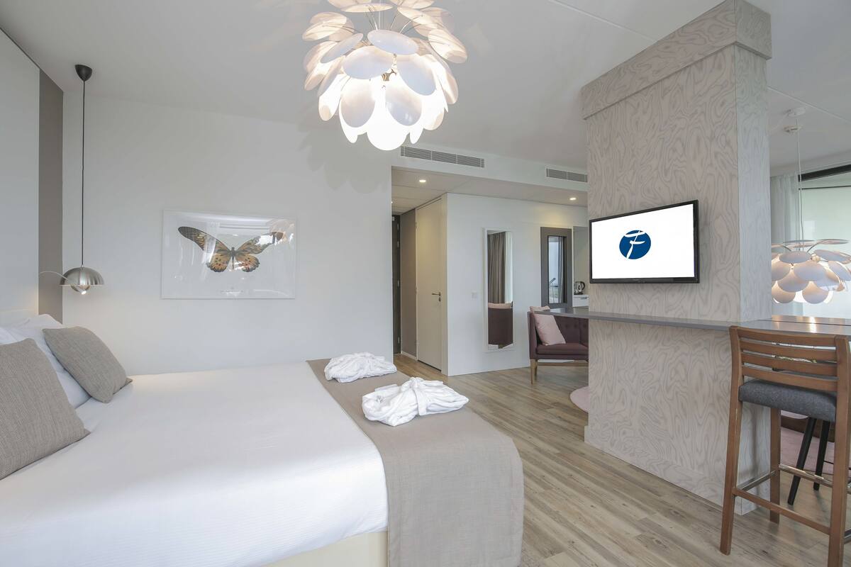 Quarto de hotel moderno com uma cama grande, televisão na parede e um pequeno bar.