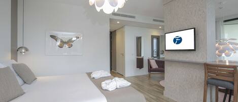 A modern hotel room with a large bed, a TV mounted on the wall, and a small bar area.