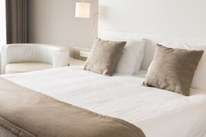A hotel room with a large bed, two pillows, a chair, and a nightstand with a lamp.