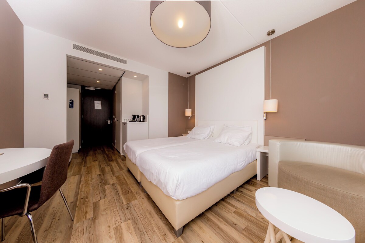 A modern hotel room with a bed, a sofa, a small table, and a chair.