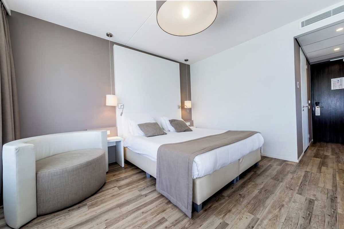 A modern hotel room with a bed, bedside tables, a round seating area, and a large mirror.