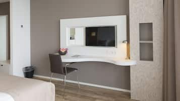 Une chambre d’hôtel moderne dotée d’un bureau incurvé, d’un téléviseur fixé au mur, d’un petit coin salon avec un fauteuil et d’une poubelle.