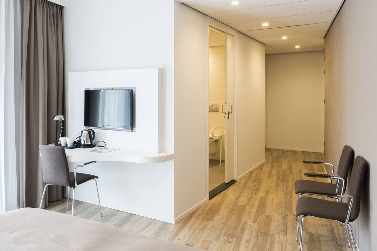 Quarto de hotel moderno com escrivaninha, cadeira e televisão.