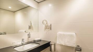 Un baño moderno con un espejo grande, un lavabo, un perchero para toallas y un cubo de basura.