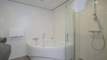Een moderne badkamer met een douchecabine van glas, een vrijstaand bad en een betegelde muur in het wit.