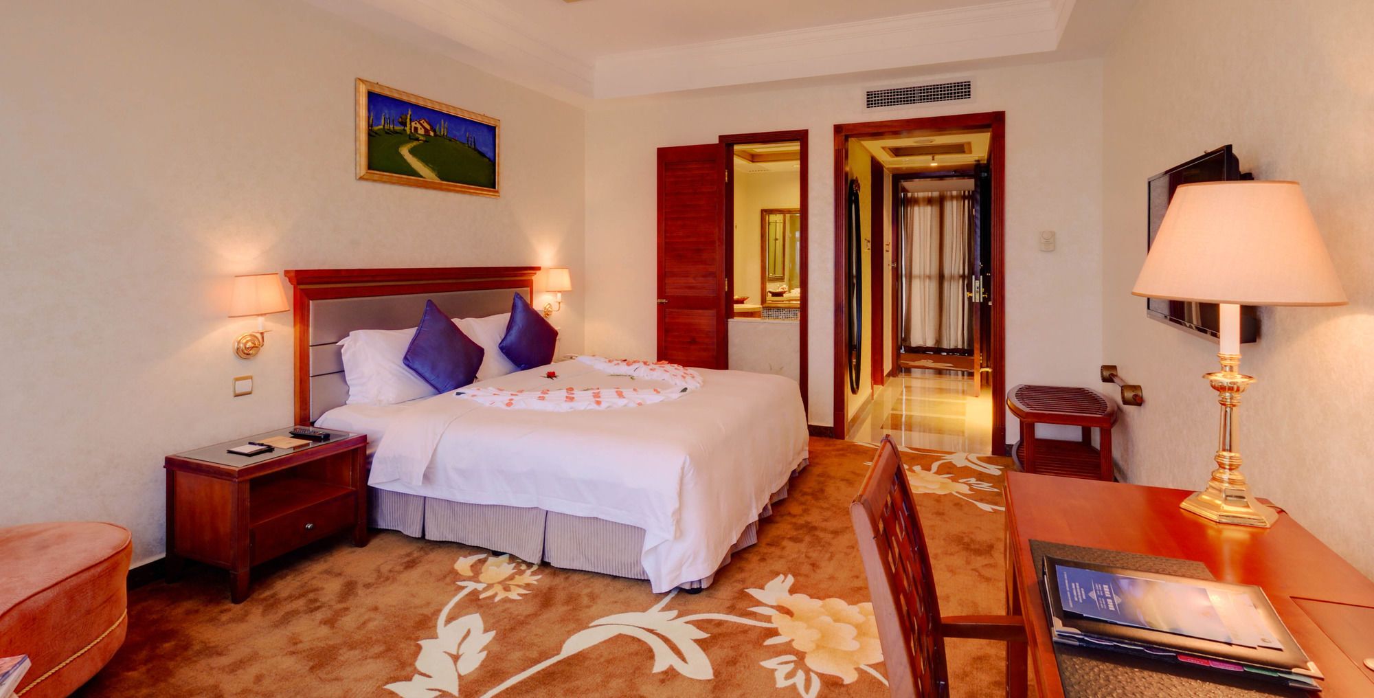 Une chambre d’hôtel avec un lit, des tables de chevet, un bureau, une chaise, une lampe et un tableau au mur.