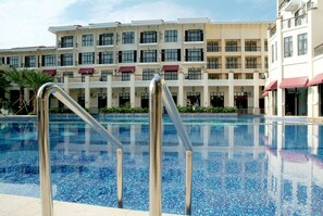 A swimming pool with metal railings in front of a multi-story hotel with balconies and awnings. - Hawana Resort Hotel (Guangzhou)