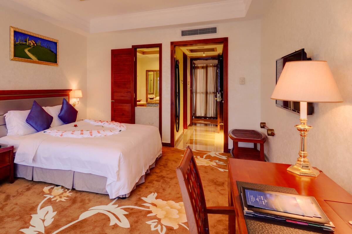 A hotel room with a bed, nightstand, desk, chair, and a lamp.