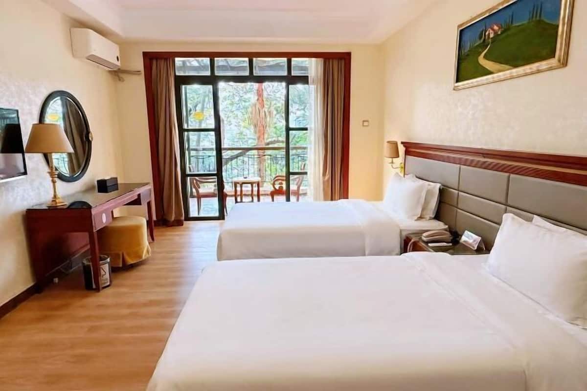 A hotel room with two beds, a desk, a chair, and a view of the outdoors.