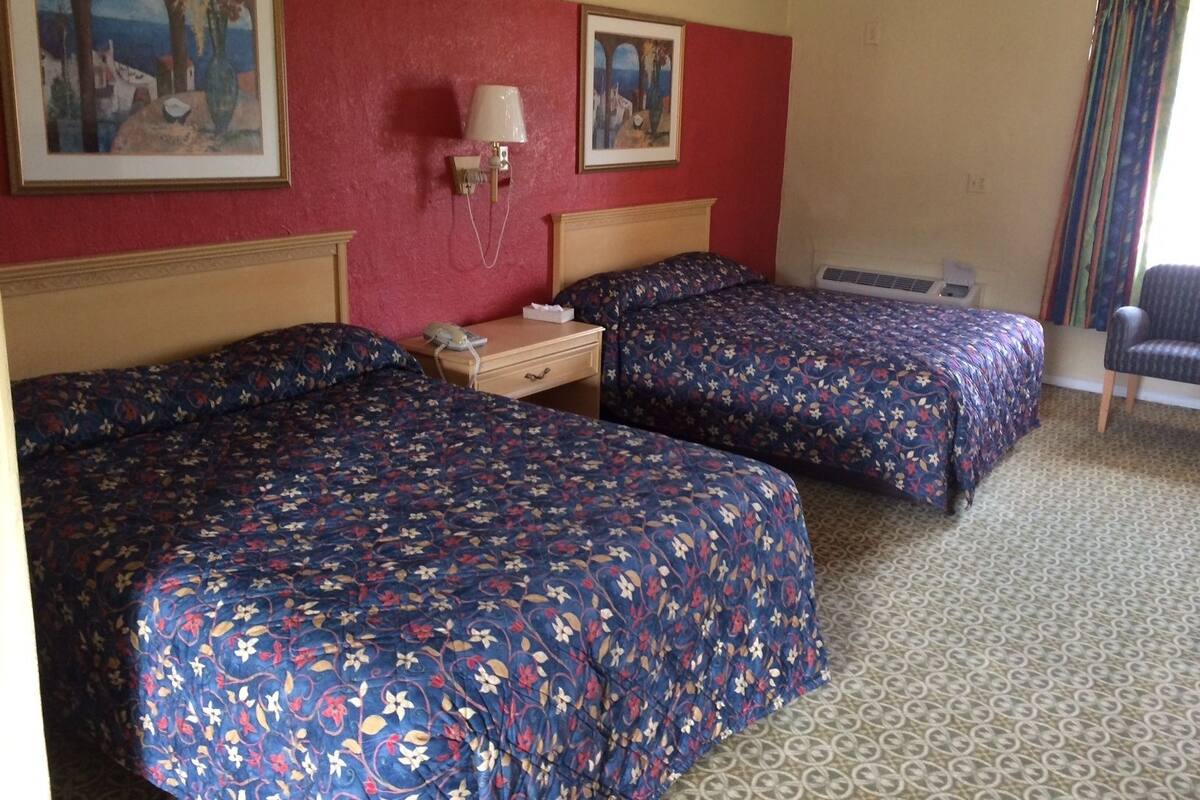 Habitación de hotel con dos camas, una mesita de noche, una lámpara y dos cuadros en la pared.