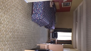 Una habitación con papel tapiz estampado, una cama con colcha floral, una ventana con cortinas y un escritorio con silla.