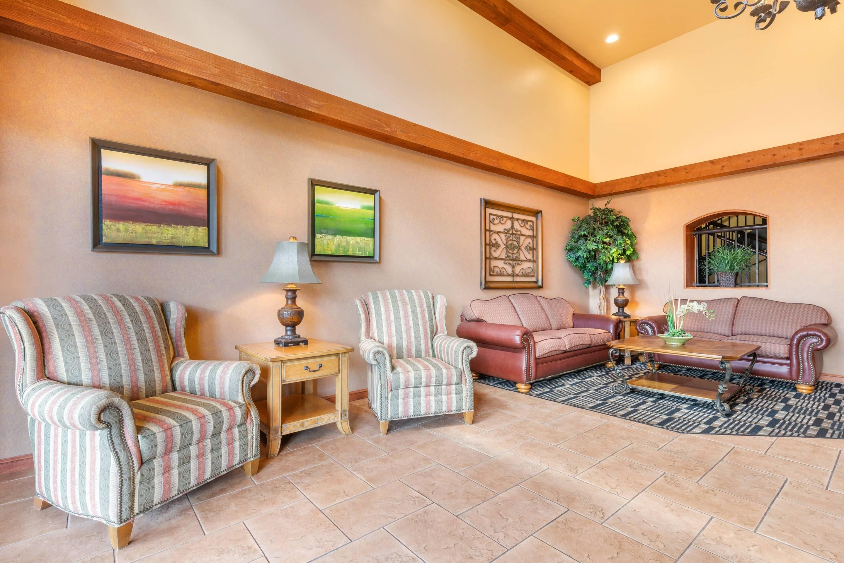 A living room with two armchairs, a sofa, a coffee table, and a rug. There are two paintings on the wall and a potted plant.