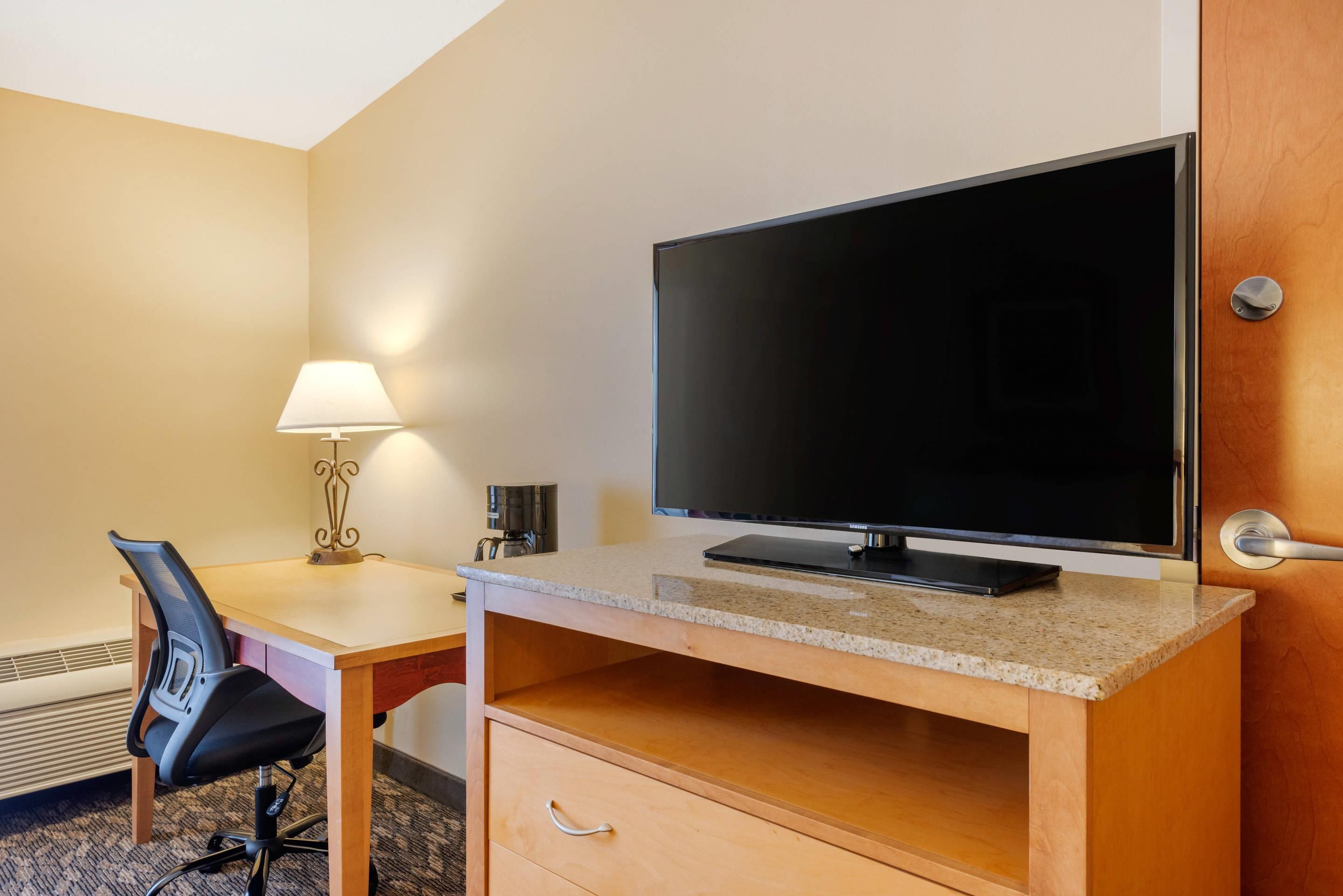 A hotel room with a desk, chair, television, lamp, and a coffee maker.