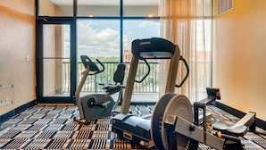 Ein Hotelzimmer mit großem Fenster, Laufband, Crosstrainer und einer Hantelbank.
