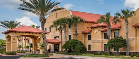 Un hotel de techo con tejas rojas, palmeras y estacionamiento.