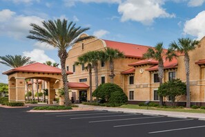 A hotel with a red-tiled roof, palm trees, and a parking lot. - Clarion Inn Ormond Beach at Destination Daytona (Ormond Beach)