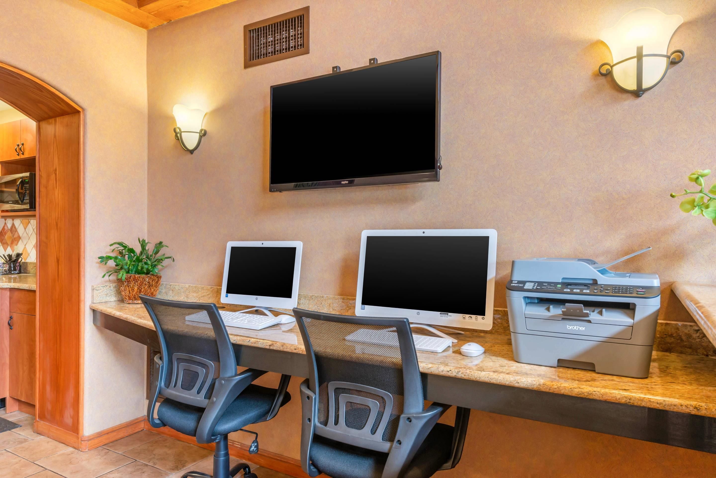 A home office with two desktop computers, a flat-screen TV, and a Brother printer on a kitchen counter.