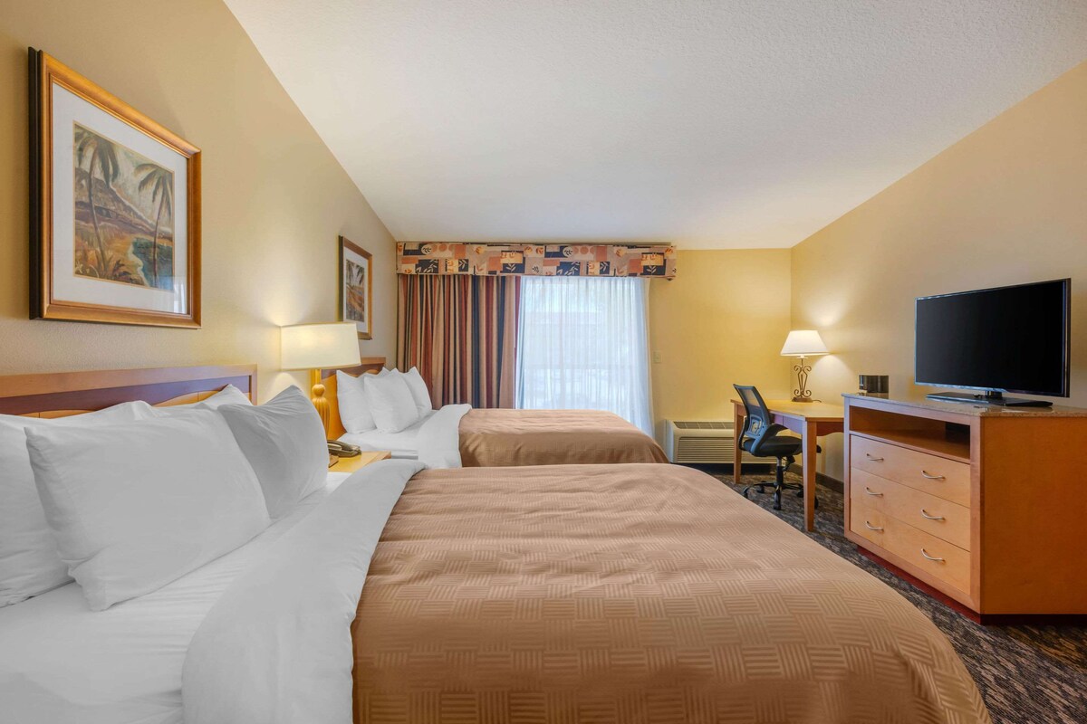 A hotel room with two beds, a desk, a chair, a television, and a window with curtains.