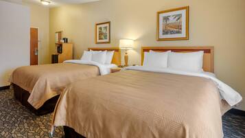 A hotel room with two beds, a nightstand, a lamp, and two framed pictures on the wall.