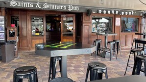 Eine Kneipe namens 'Saints & Sinners Pub' mit Barbereich, Hockern und einem Tisch mit grünem Muster.