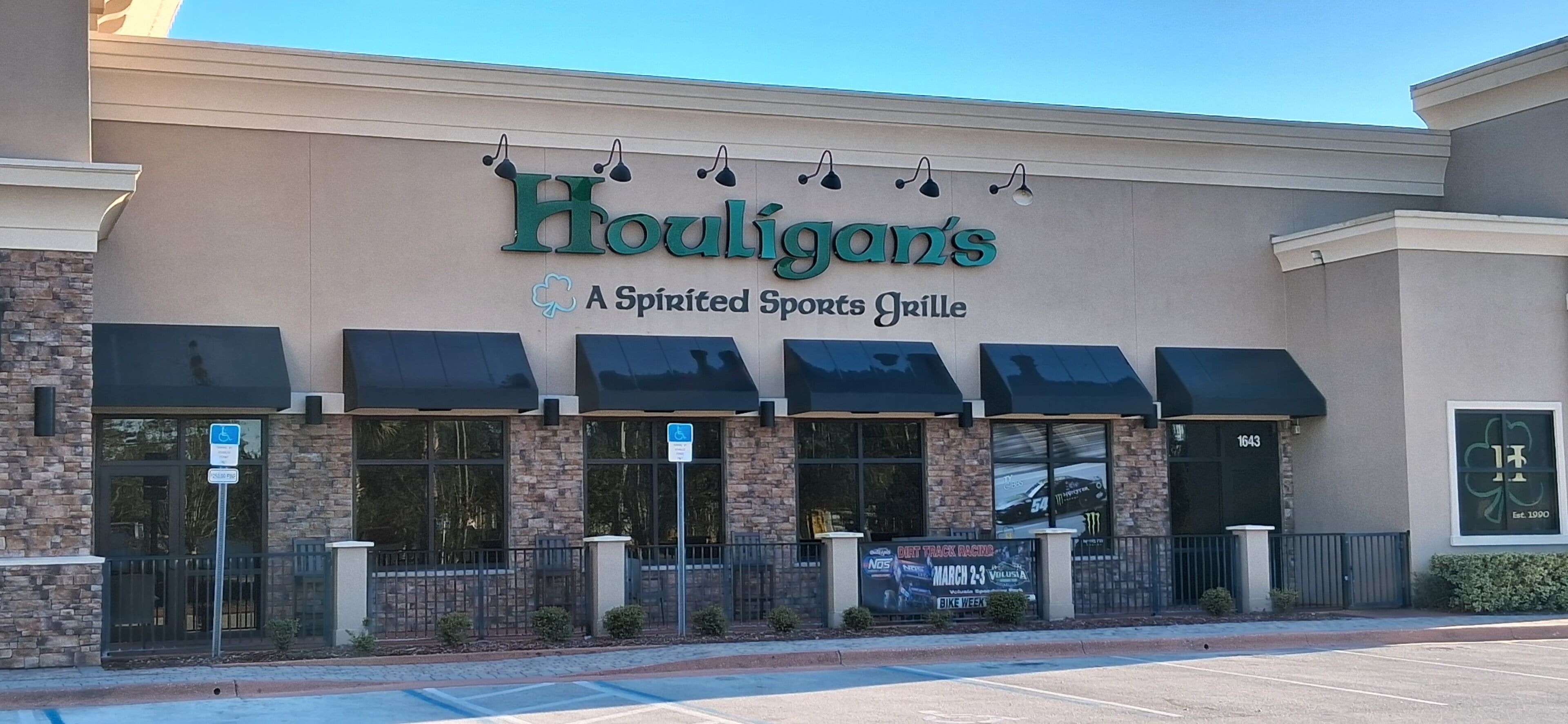 A building with a sign reading 'Houligan's A Spirited Sports Grille' and a parking lot in front.
