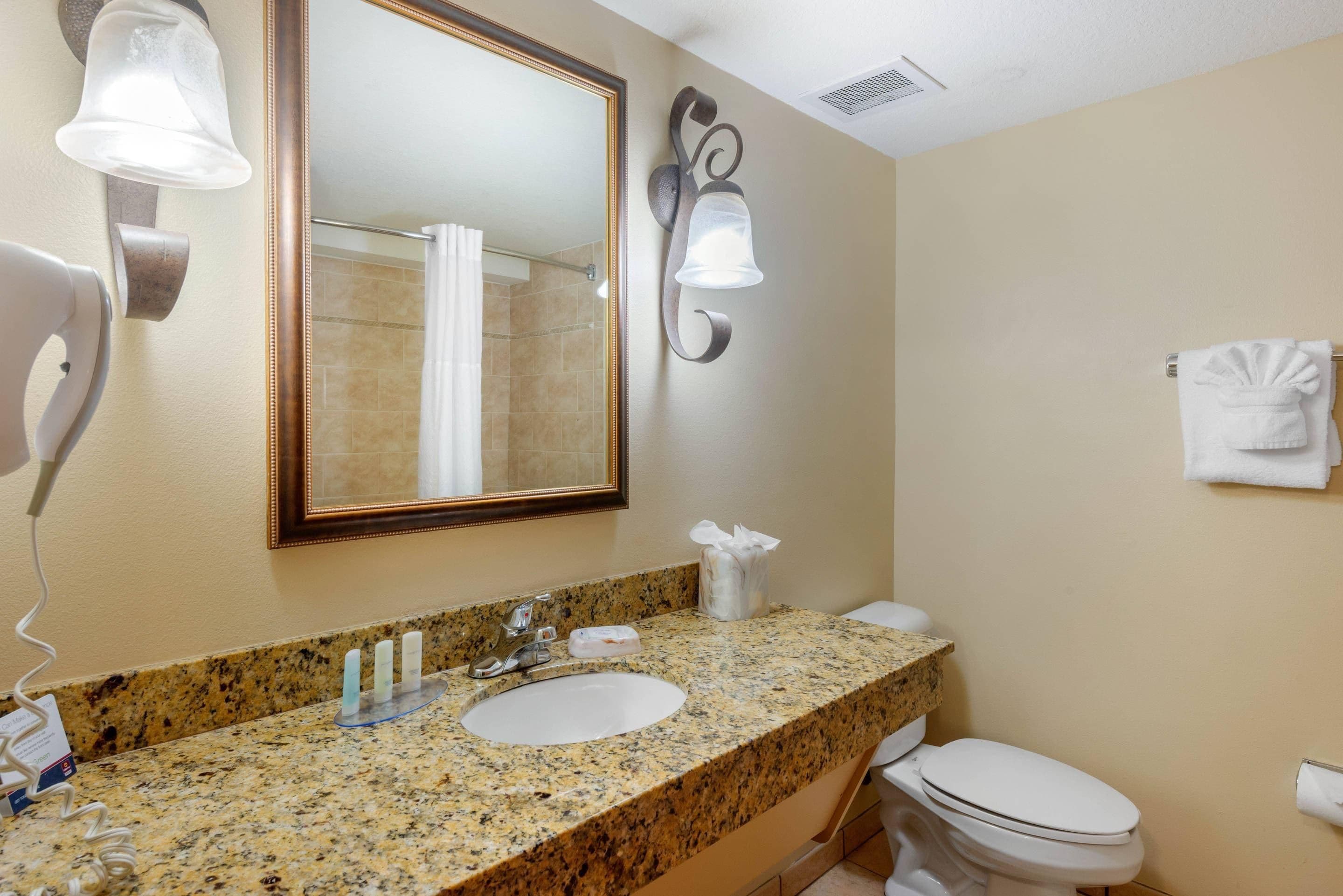 A bathroom with a granite countertop, a sink, a toilet, a mirror, and a towel rack.